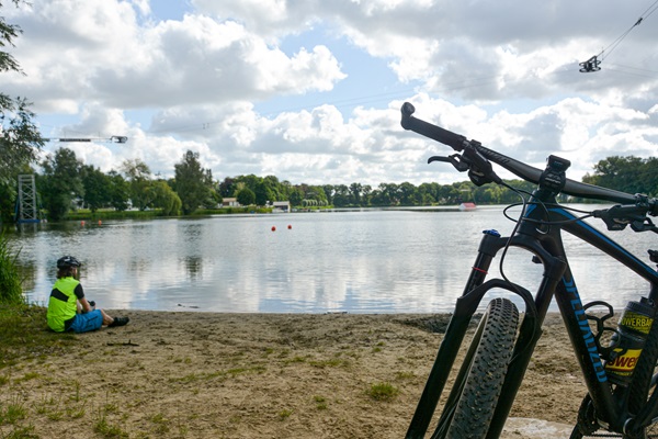 Mountainbike steht im Vordergrund, während der Fahrer das Wasser genießt