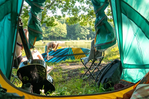 Junge bereitet sich zum Stand-Up-Paddling vor, während seine Freundin vor dem Zelt auf einem Campingplatz sitzt während das Übernachten in Roermond